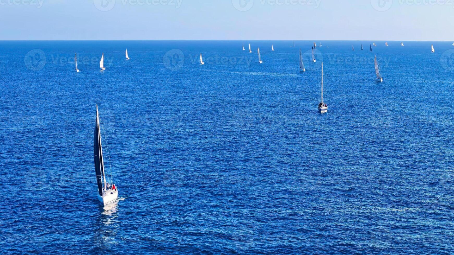 Sailing adventure unfolds on tranquil waters as multiple boats glide across the deep blue sea under a clear sky photo