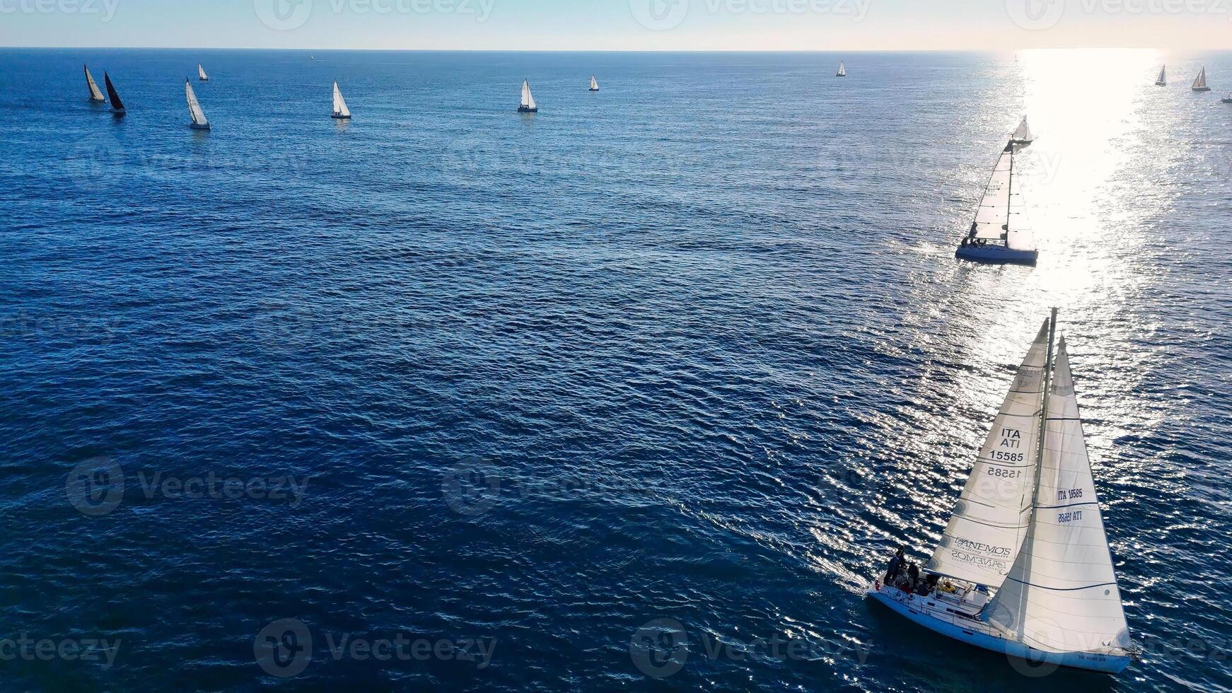 Sailing along the coastline at sunset, a vibrant regatta unfolds amidst the shimmering waves photo