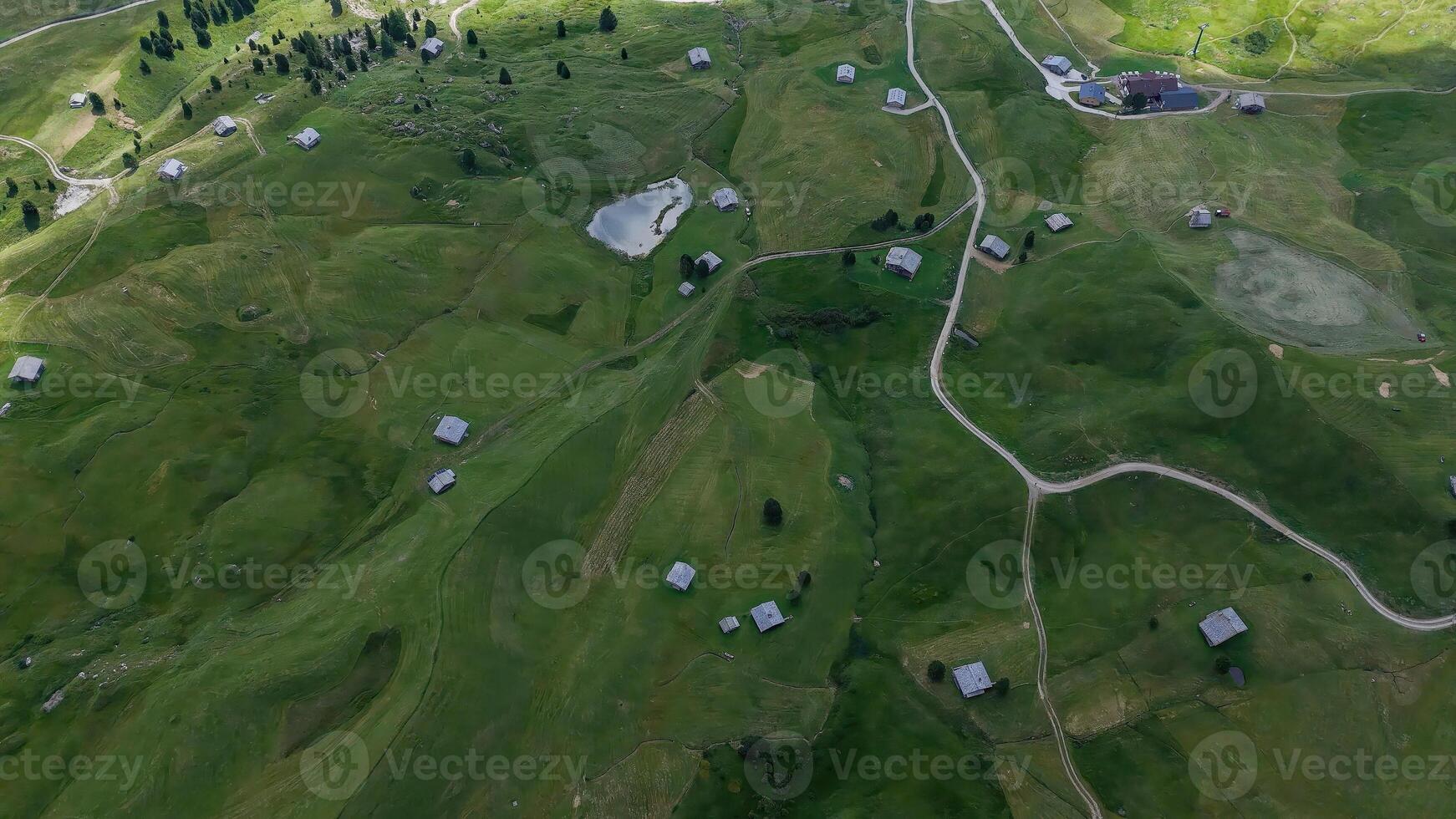 Aerial view capturing lush green fields dotted with rustic cabins under a bright sky in a serene countryside location photo