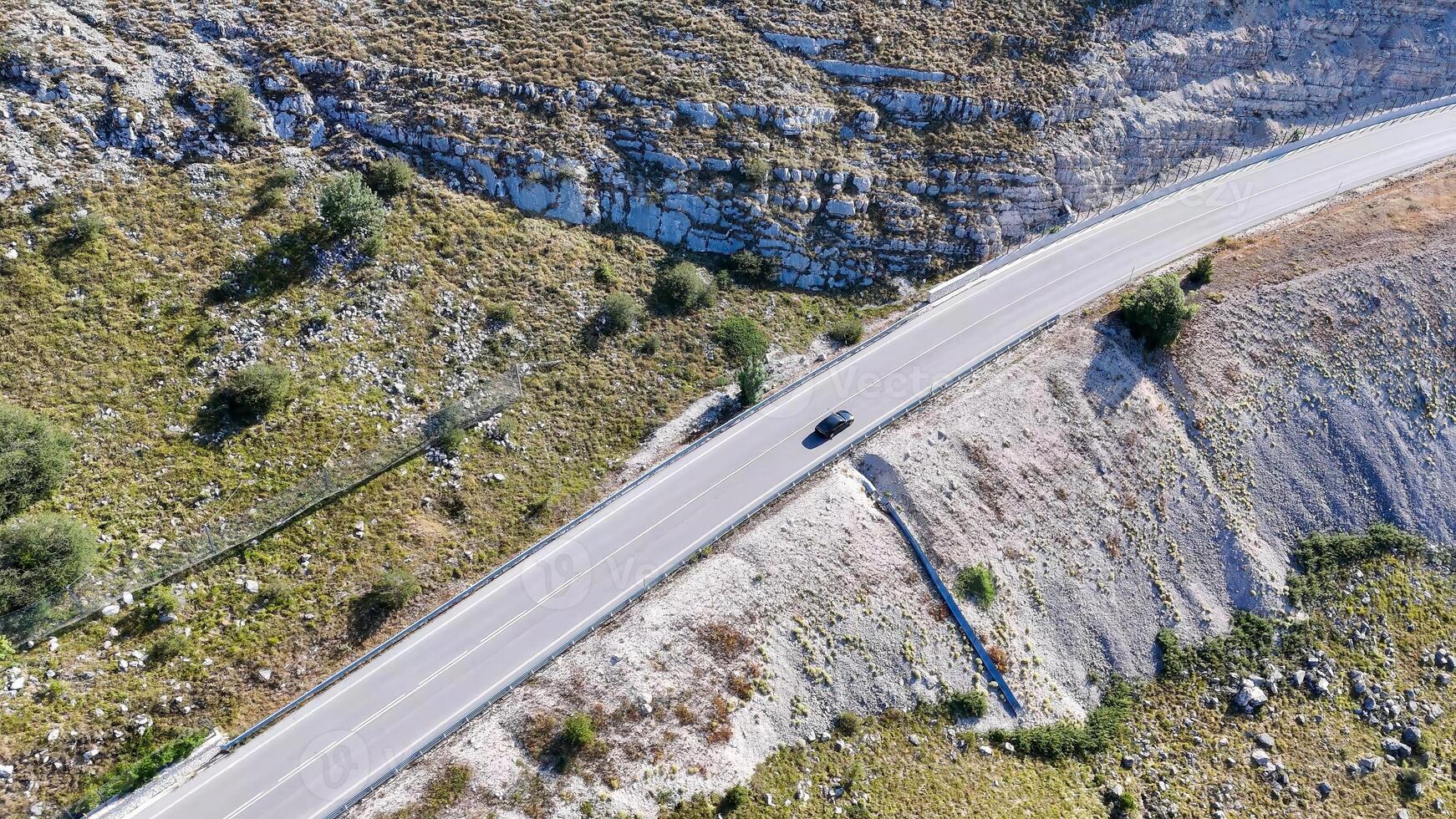 Scenic highway winds through rocky terrain with a solitary car under clear blue skies in a remote landscape photo