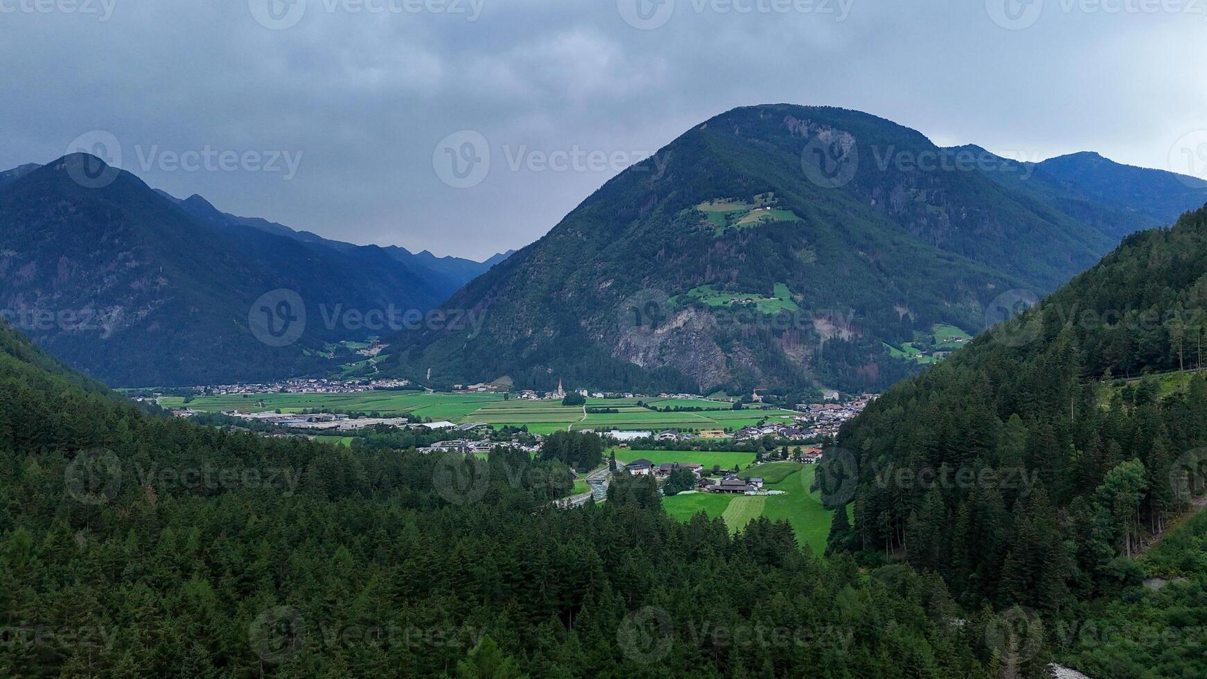 Breathtaking view of green valleys and majestic mountains near a serene village during a cloudy afternoon in the Alps photo
