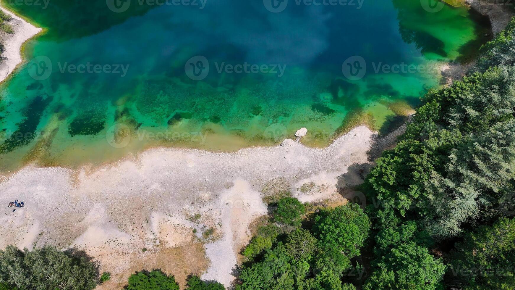 Vibrant emerald waters of a secluded lake surrounded by lush greenery and sandy shores create a serene escape into nature photo