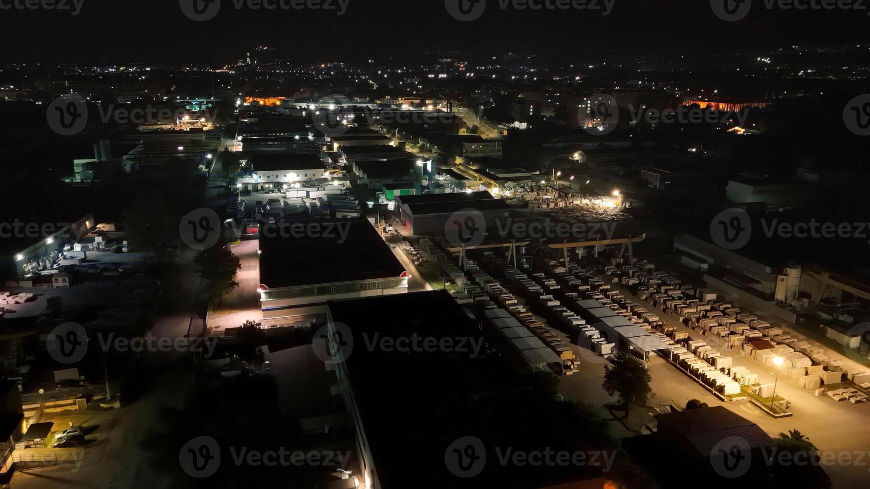 Urban nightscape showcasing vibrant industrial activity illuminated by glowing lights and a serene backdrop of distant hills photo