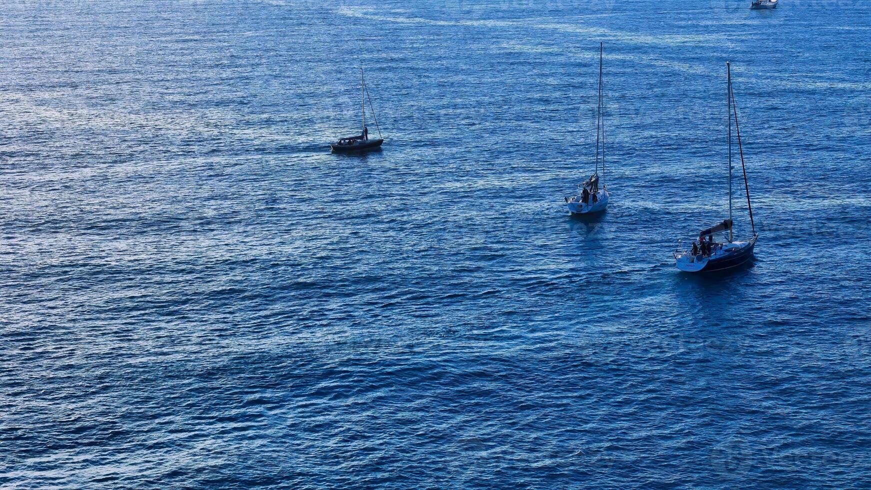 Sailboats dance on vibrant azure waters under the warm glow of a setting sun photo