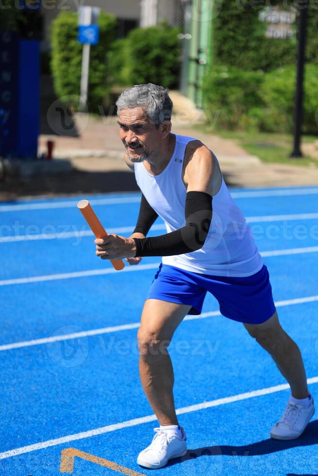 Senior Asian athlete is practicing running with the relay baton in the professional blue track for professional exercise, sport training workout and healthy for longevity concept photo