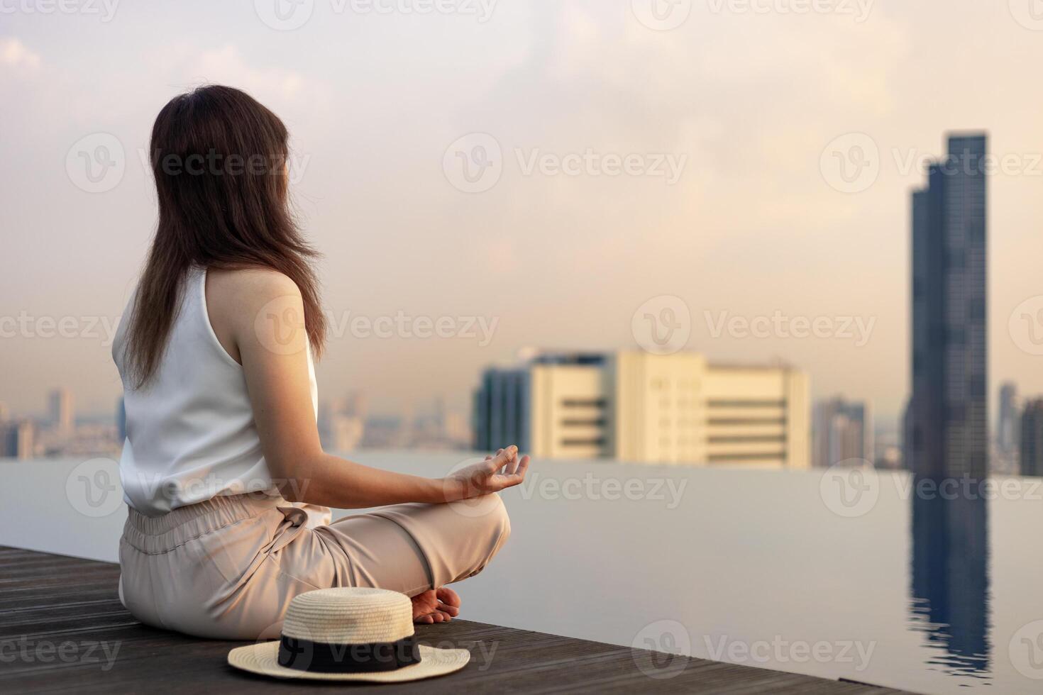Back of woman relaxingly practicing meditation at the swimming pool rooftop with view of urban skyline building to attain happiness from inner peace wisdom photo