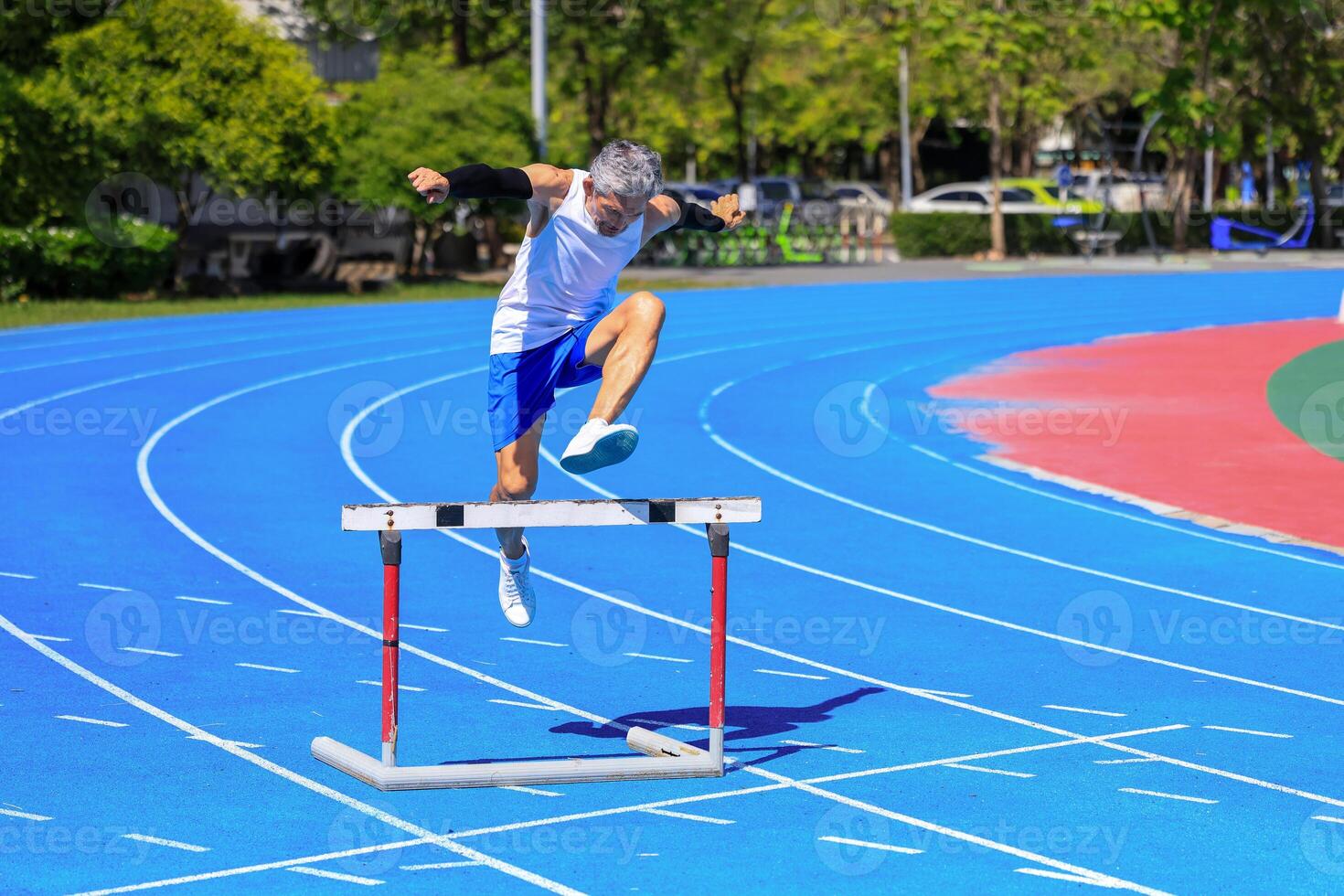 Asian senior athlete is practicing hurdling running in the professional blue track for professional exercise, sport training workout and healthy for longevity photo