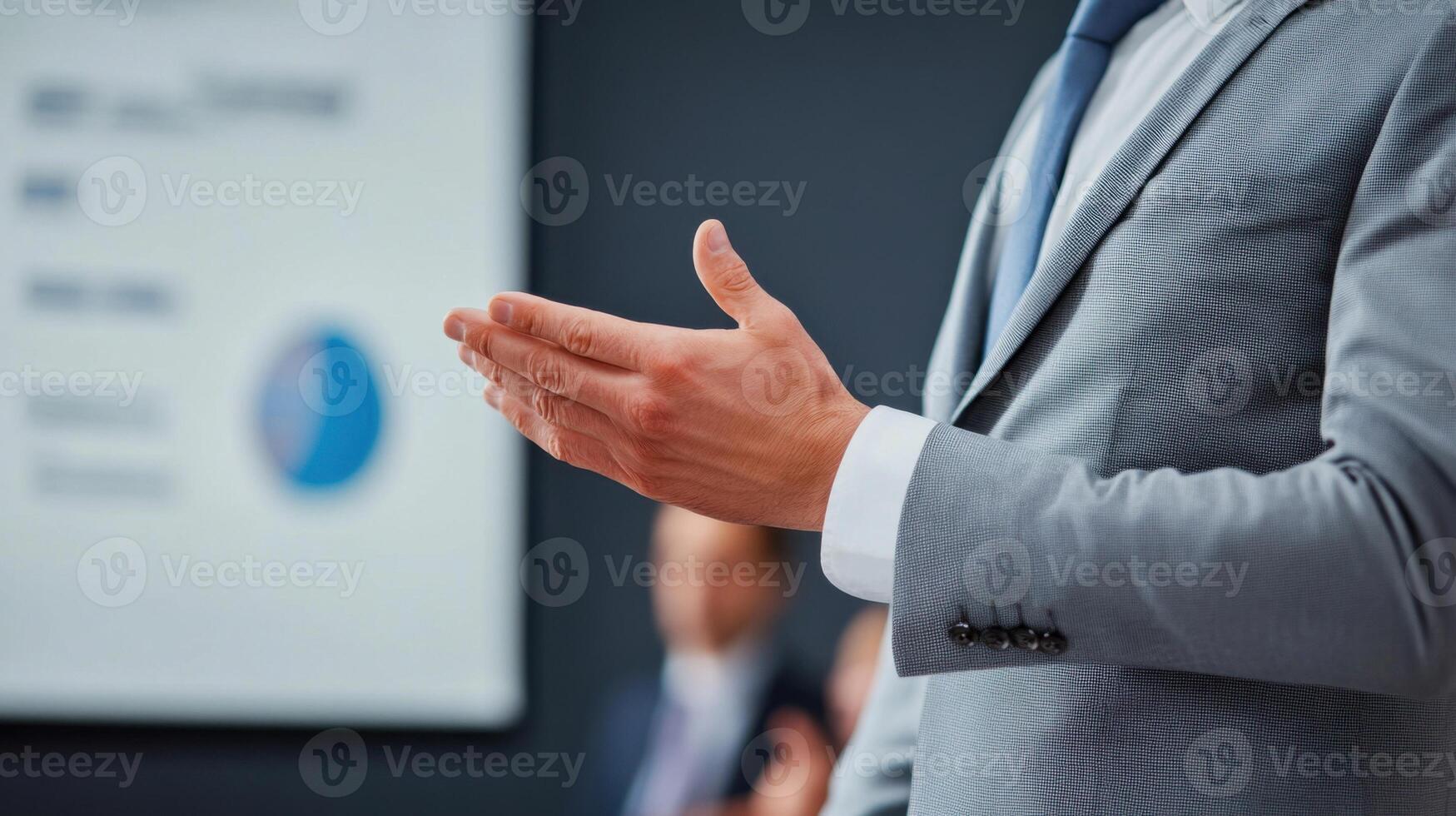 Cropped view of businessman in gray suit gesturing with hand during presentation, with blurred chart or graph in background photo