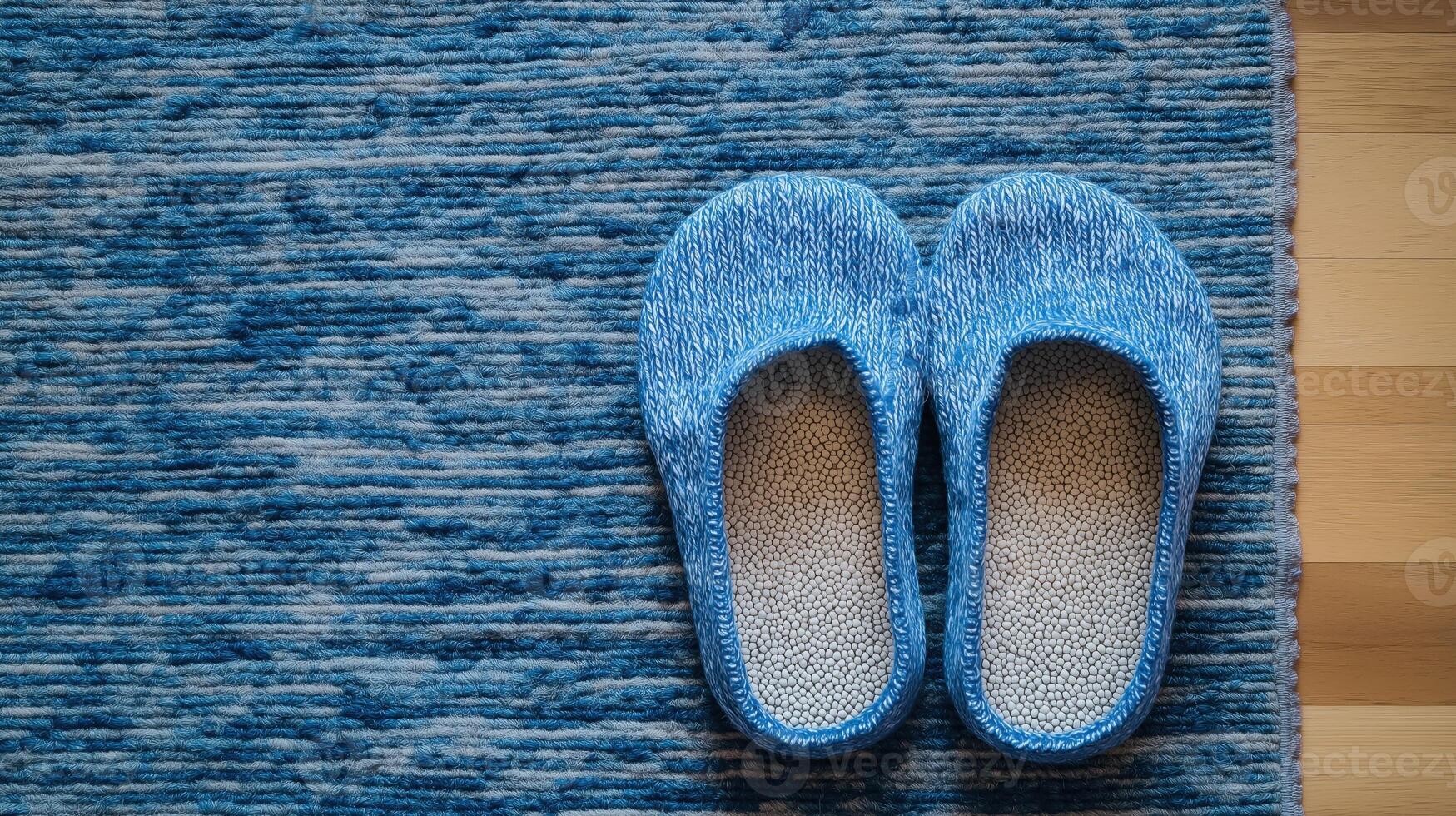 Comfortable blue fuzzy slippers on striped blue rug with textured surface, top view photo