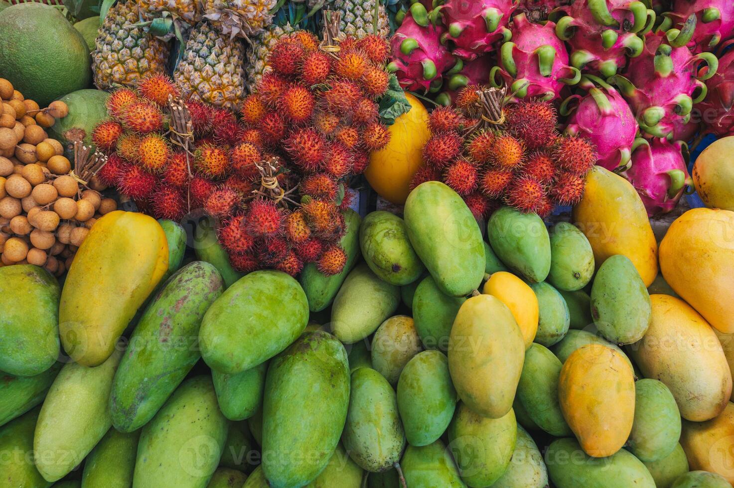 assortment of various tropical exotic Asian fruits on counter in a store in Vietnam. Vietnamese yellow and green mangoes, dragon fruit and rambutan photo