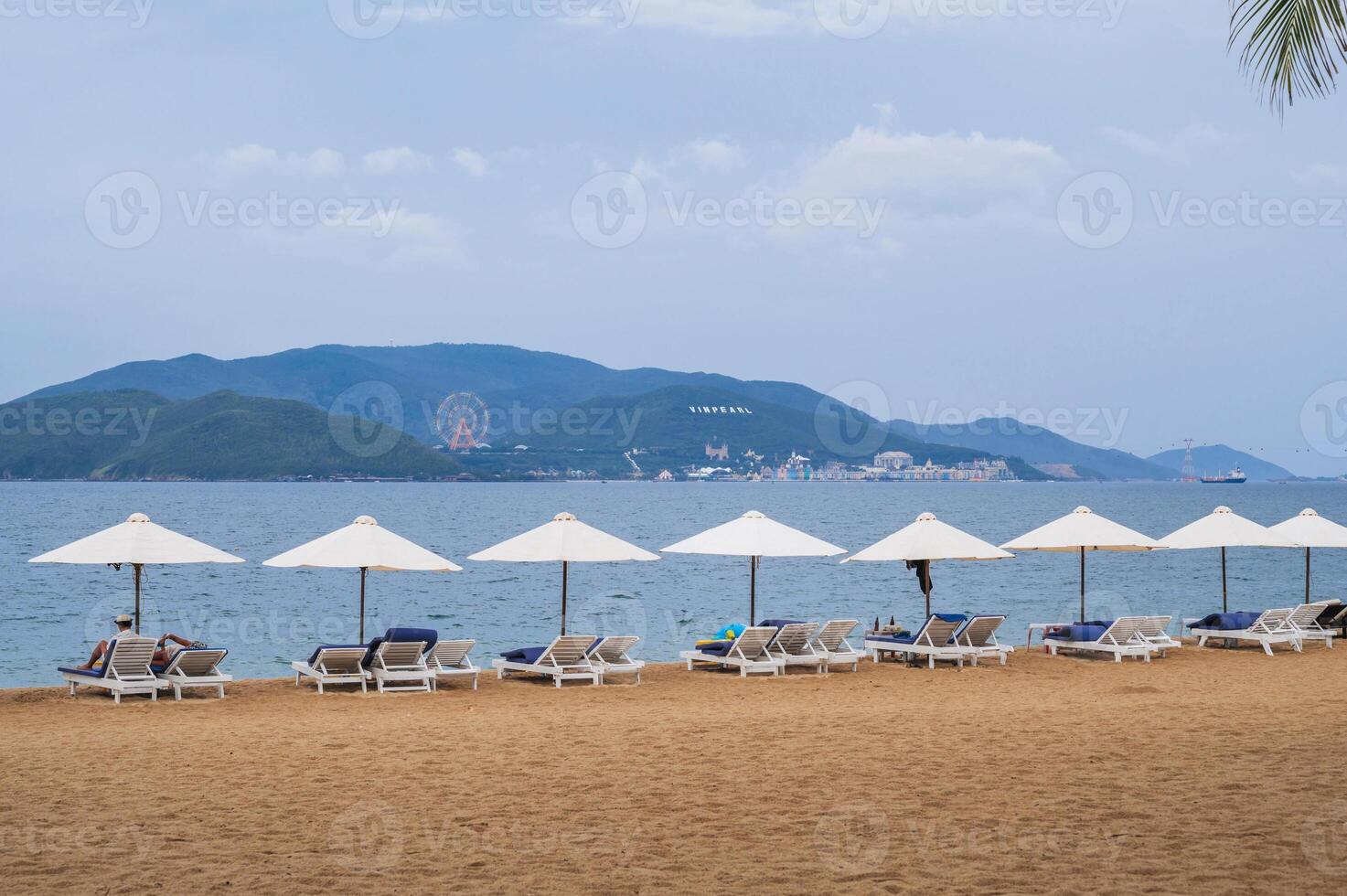 sandy beach with tourists relaxing under beach umbrellas by sea in Nha Trang resort in Vietnam in summer cloudy day photo
