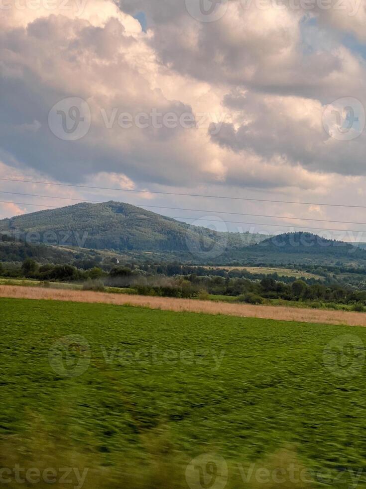 Green field stretching towards majestic mountains under cloudy sky photo