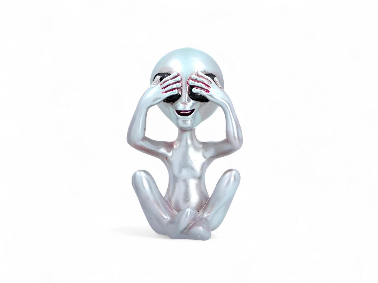 An alien figurine sitting on the floor with its hands over its eyes photo