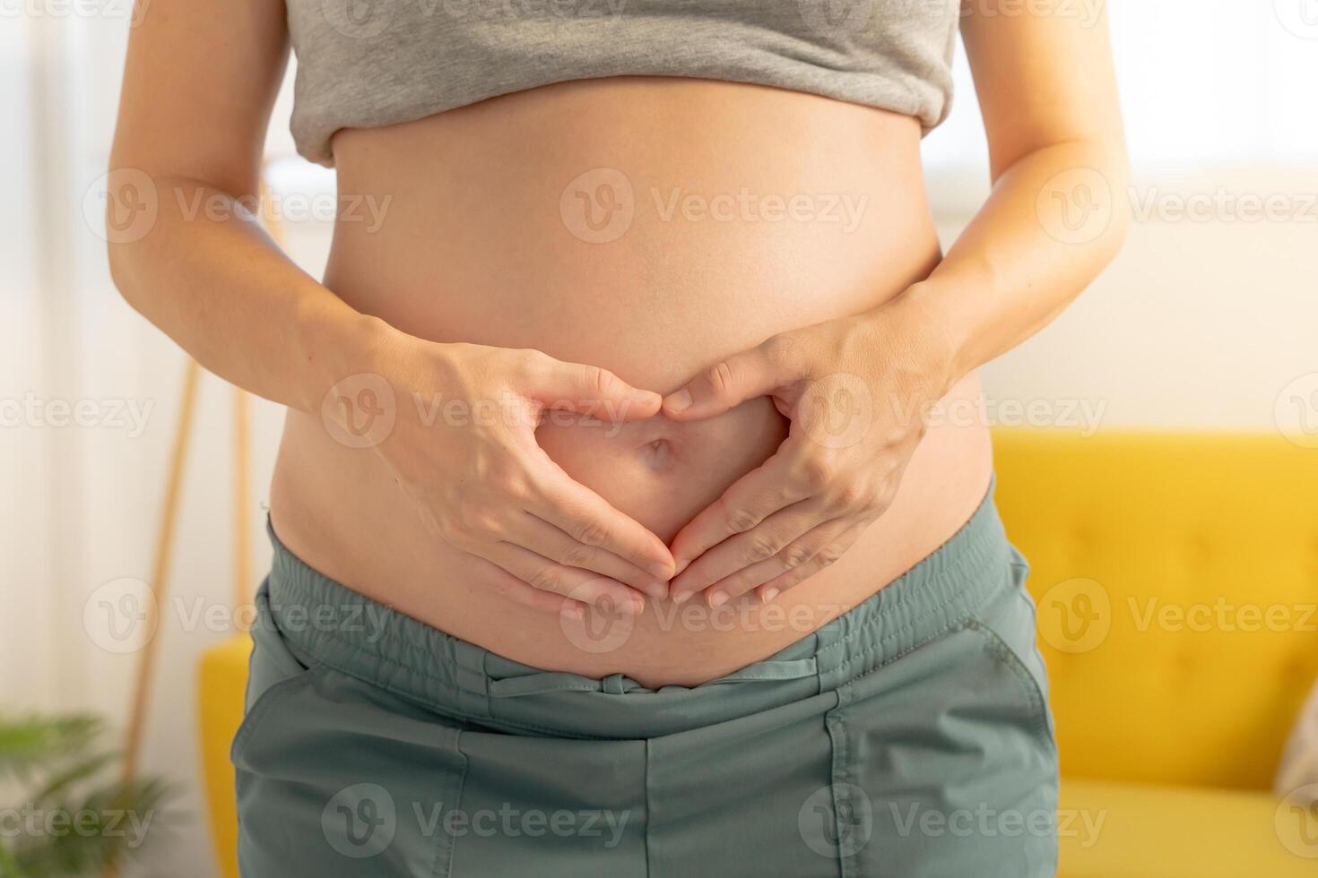 Pregnant woman forms a heart shape with her hands on her belly, symbolizing love and anticipation. photo