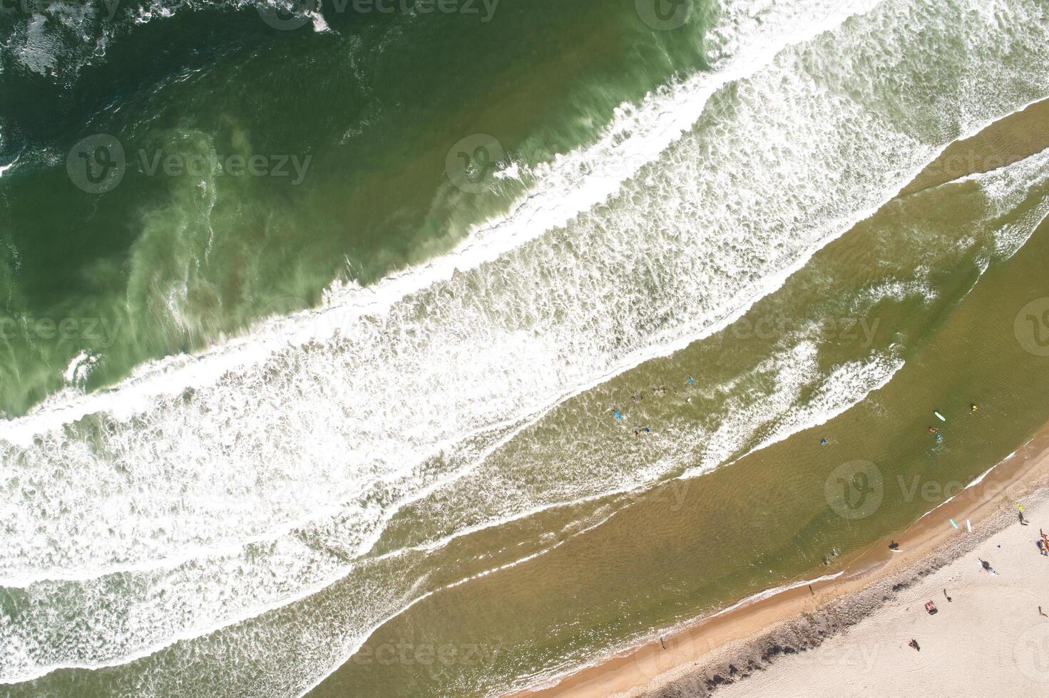 top down view of sandy beach with people and waves drone top down shot of waves breaking with people swimming photo