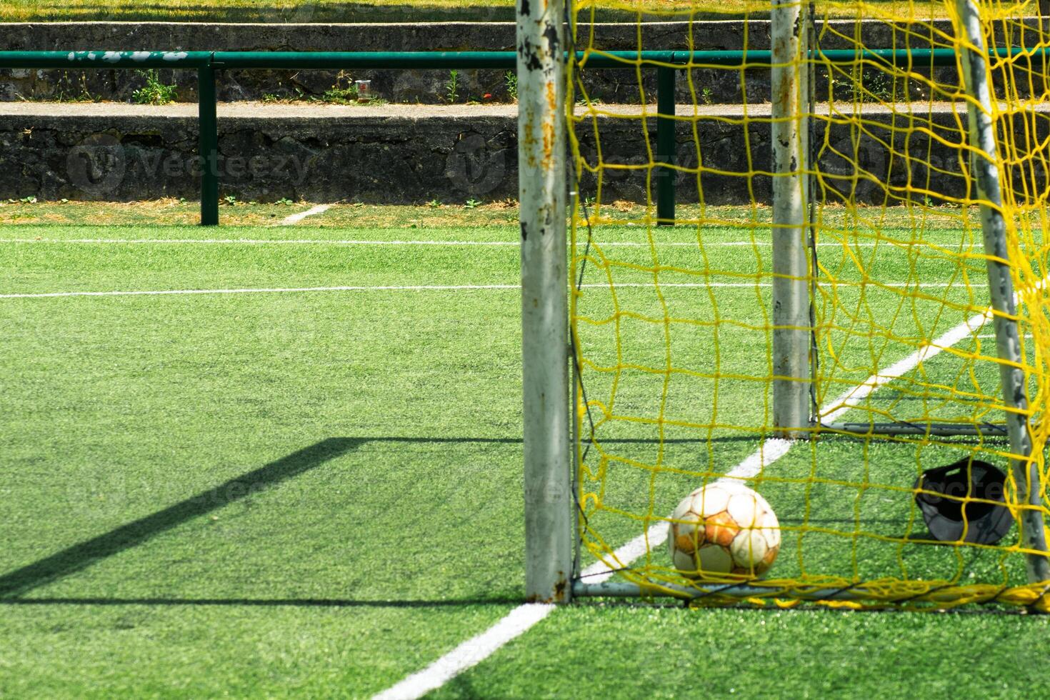 detail of a soccer ball inside a yellow goal on a green pitch, football goal with ball inside the yellow net photo