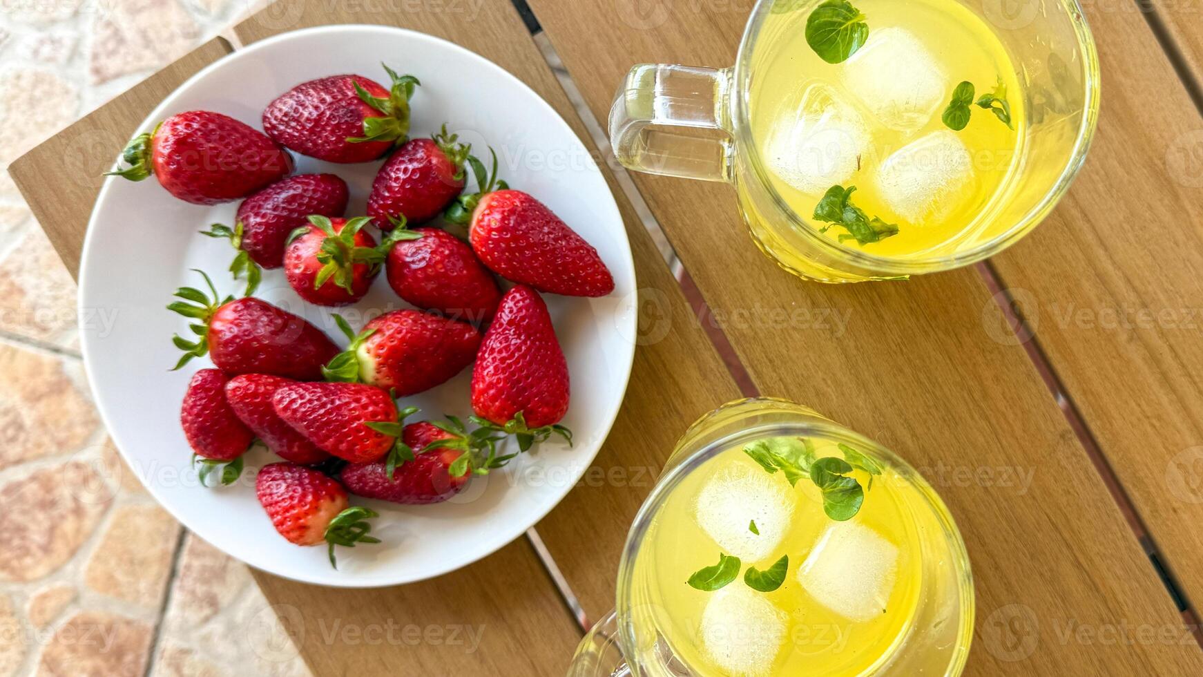 Fresh strawberries on a white plate with lemon mint iced tea, perfect for summer refreshment and garden parties photo