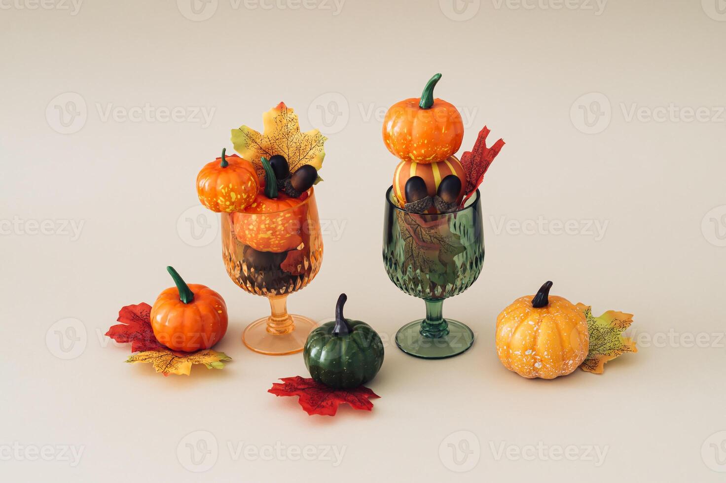 Autumn scene of two cocktail glasses full of colorful autumn leaves, pumpkins and nuts on beige background. Minimal creative Fall party concept. Festive holiday layout. photo