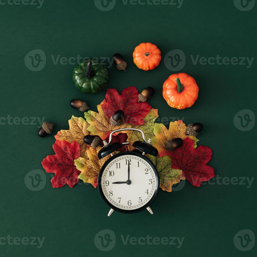 Autumn composition made with colorful autumn leaves, pumpkins, nuts and retro alarm clock on green background. Creative autumn time concept. Fall aesthetic. Flat lay style. Top view. photo