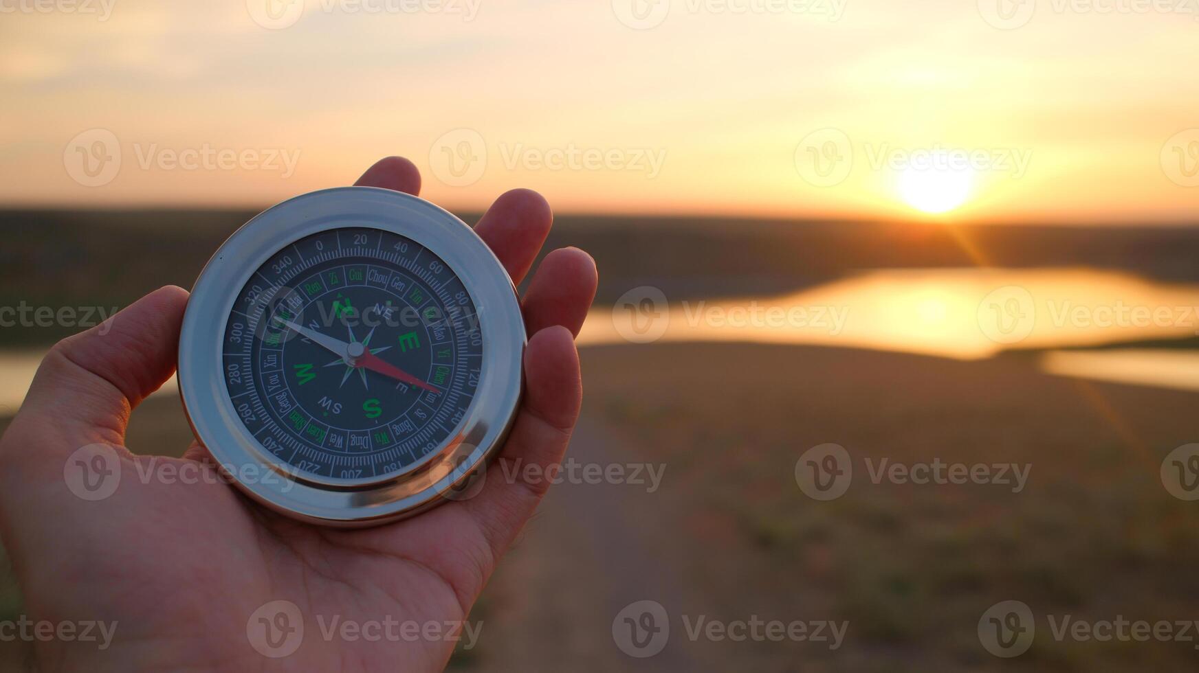 Hand holding compass during sunset over river landscape representing navigation and exploration concepts photo