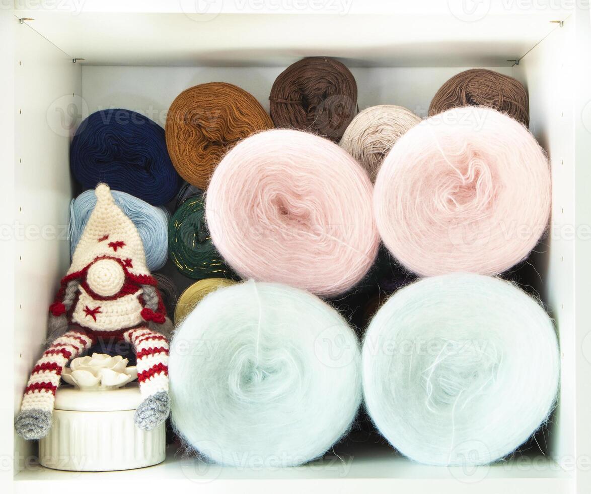 Colorful yarn balls and adorable crochet gnome sitting in organized craft room closet photo
