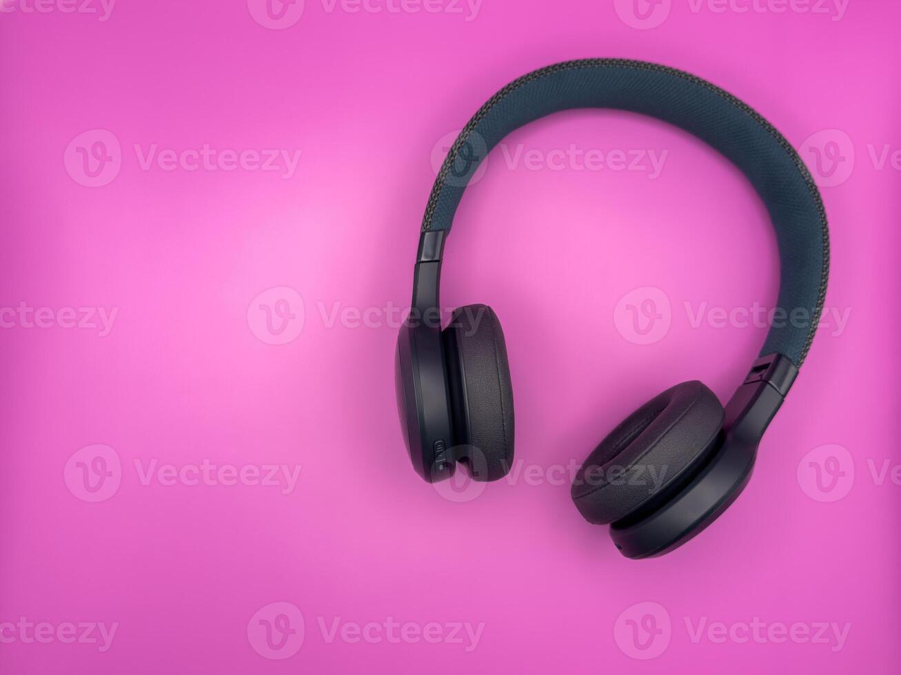 Green earphones with soft earbuds and a soft headband are lying on the right side of the image on a pink background photo