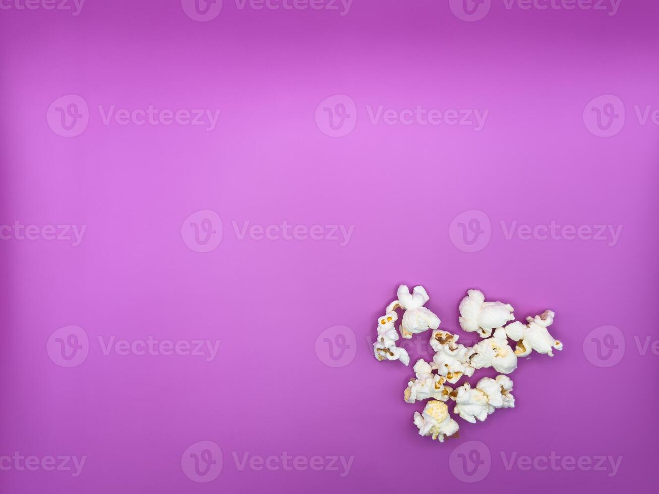 White salted popcorn scattered on purple background right corner bottom view from above photo