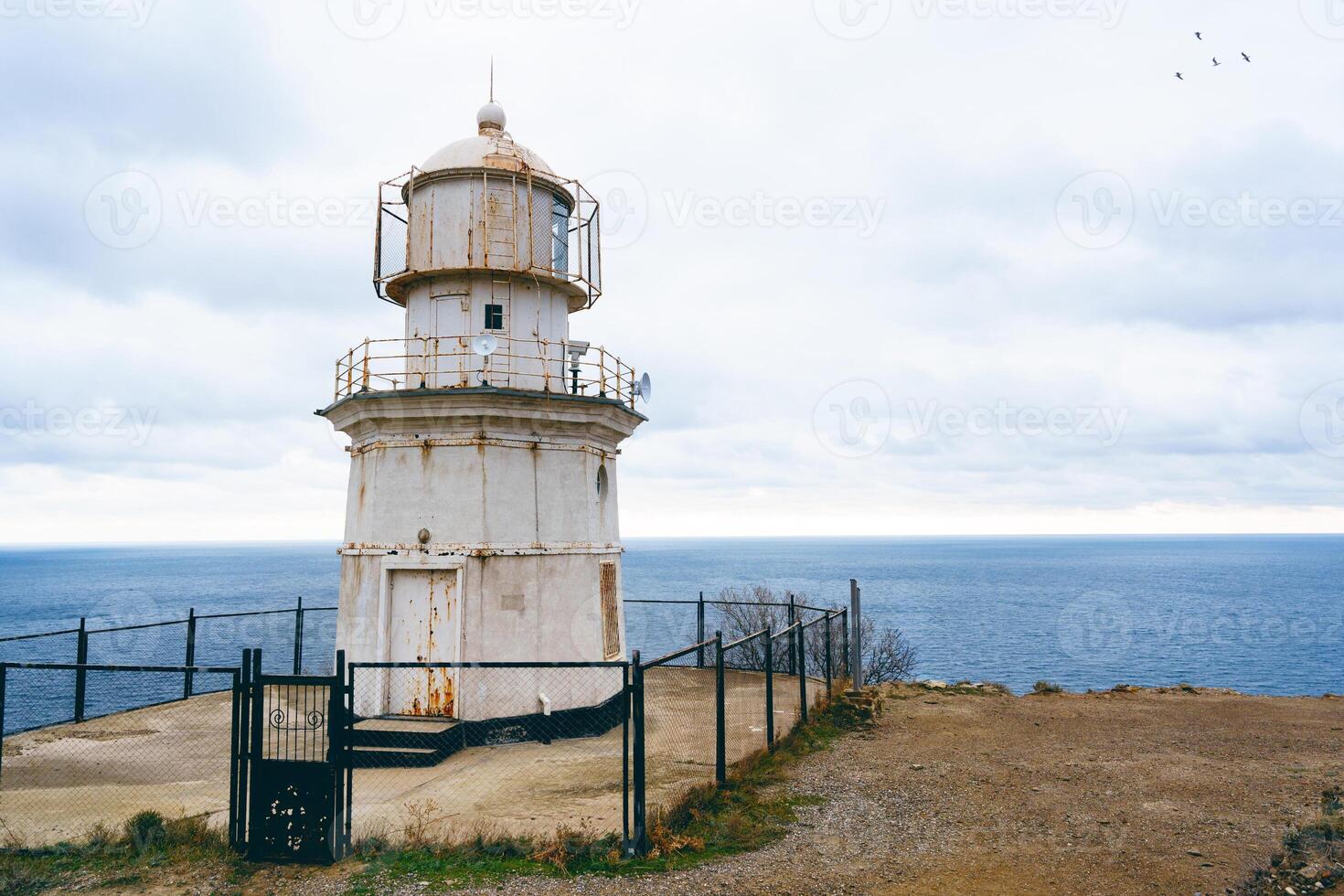 Historic lighthouse standing on a cliff overlooking the ocean under a cloudy sky photo