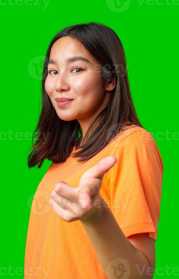 Young woman wearing an orange shirt poses confidently against a bright green background inviting viewers to engage photo