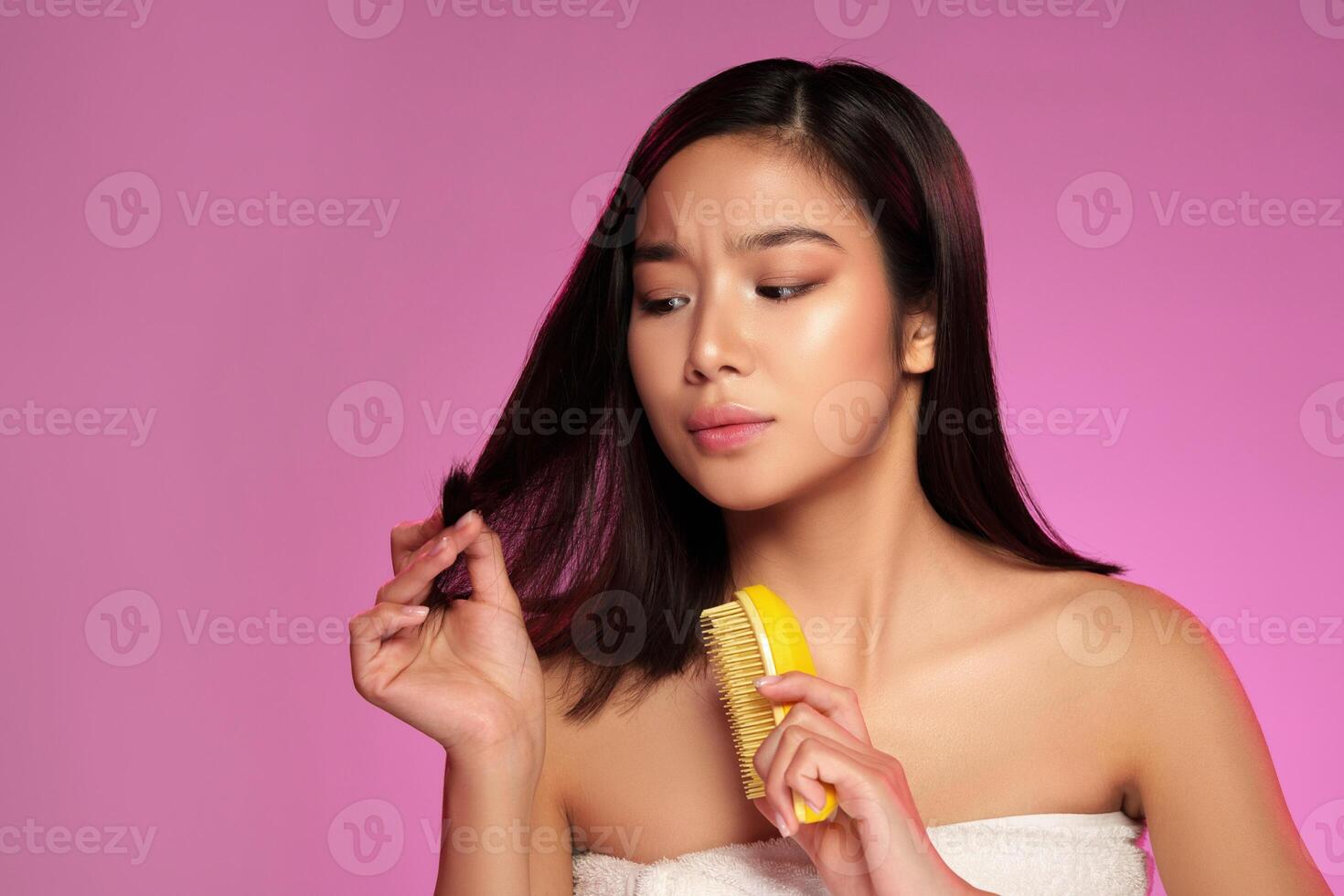Woman styling her hair with a comb while looking at it against a pink background in a beauty-focused setting photo