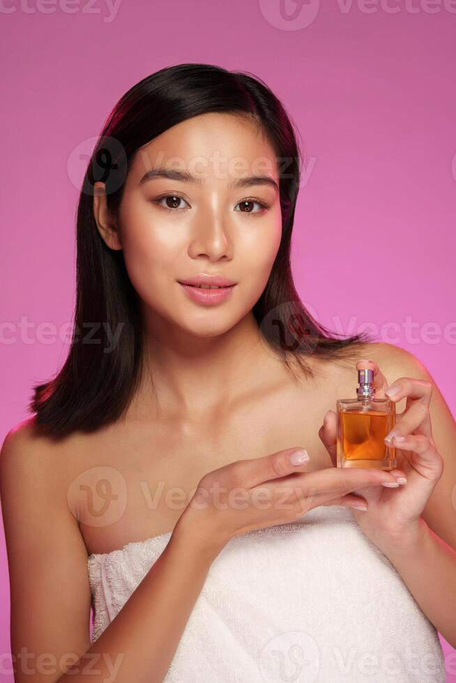 Model showcases perfume in a soft pink setting while wrapped in a towel photo