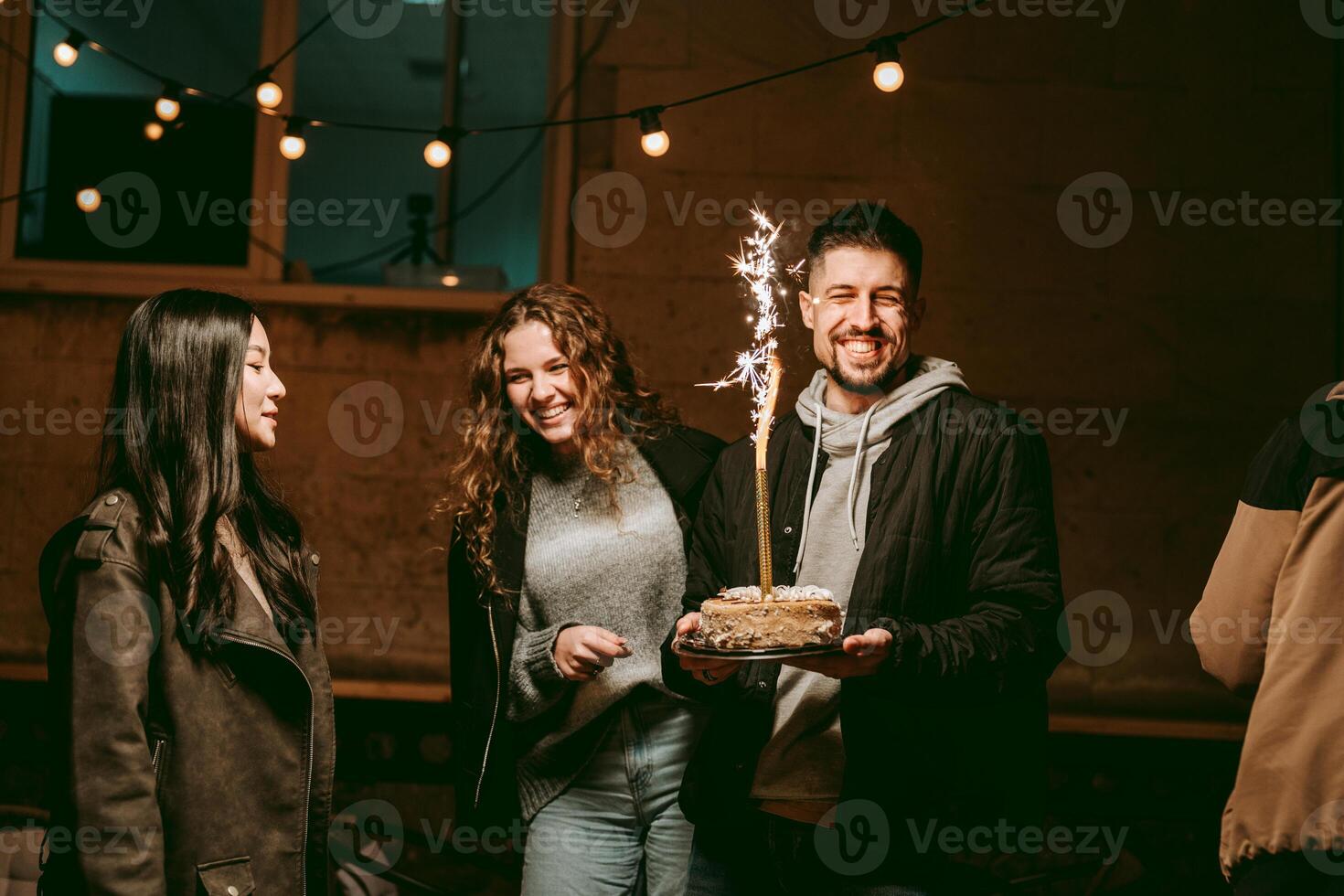 Friends celebrate a birthday with a cake featuring sparklers in a cozy indoor setting during the evening photo