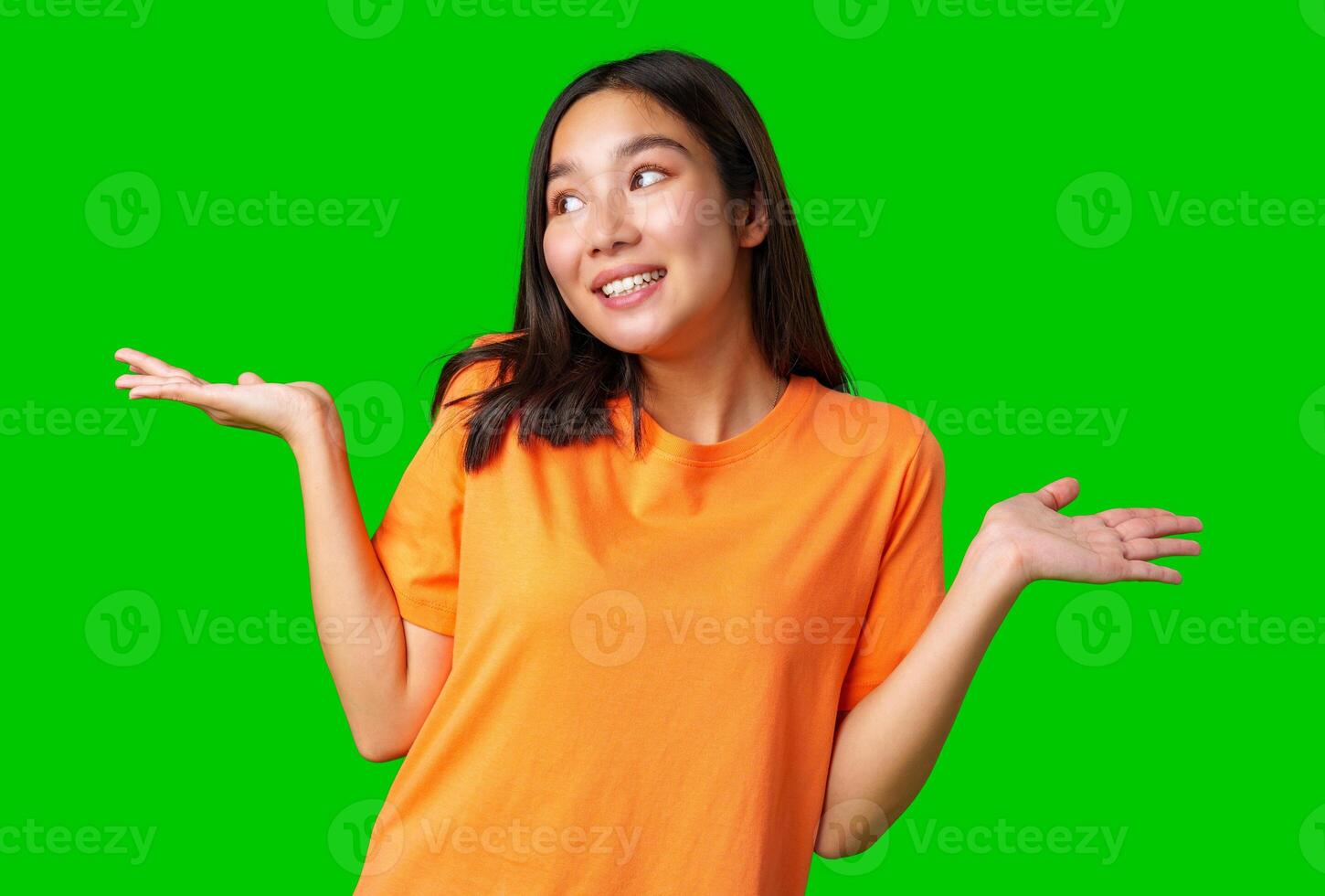 Young woman in orange shirt stands with hands raised, displaying a playful expression against a green background photo