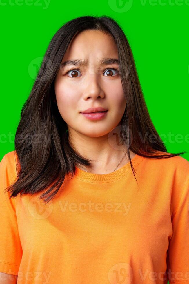 Young woman with surprised expression wears orange shirt on bright green background photo