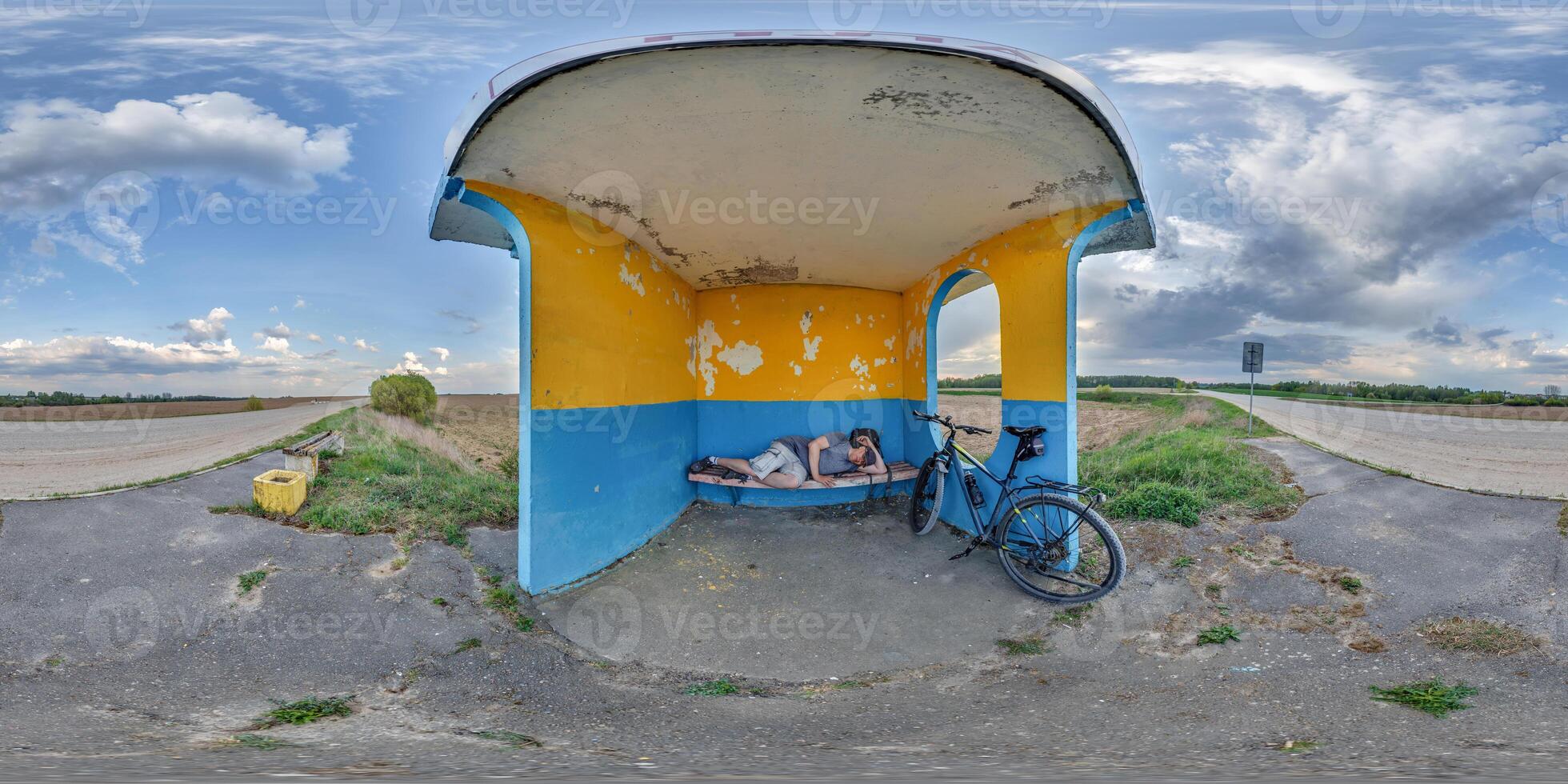 spherical seamless 360 hdri panorama inside empty concrete bus stop painted blue and yellow with tired or homeless person sleeping on bench near a bicyclein equirectangular projection, VR AR content photo
