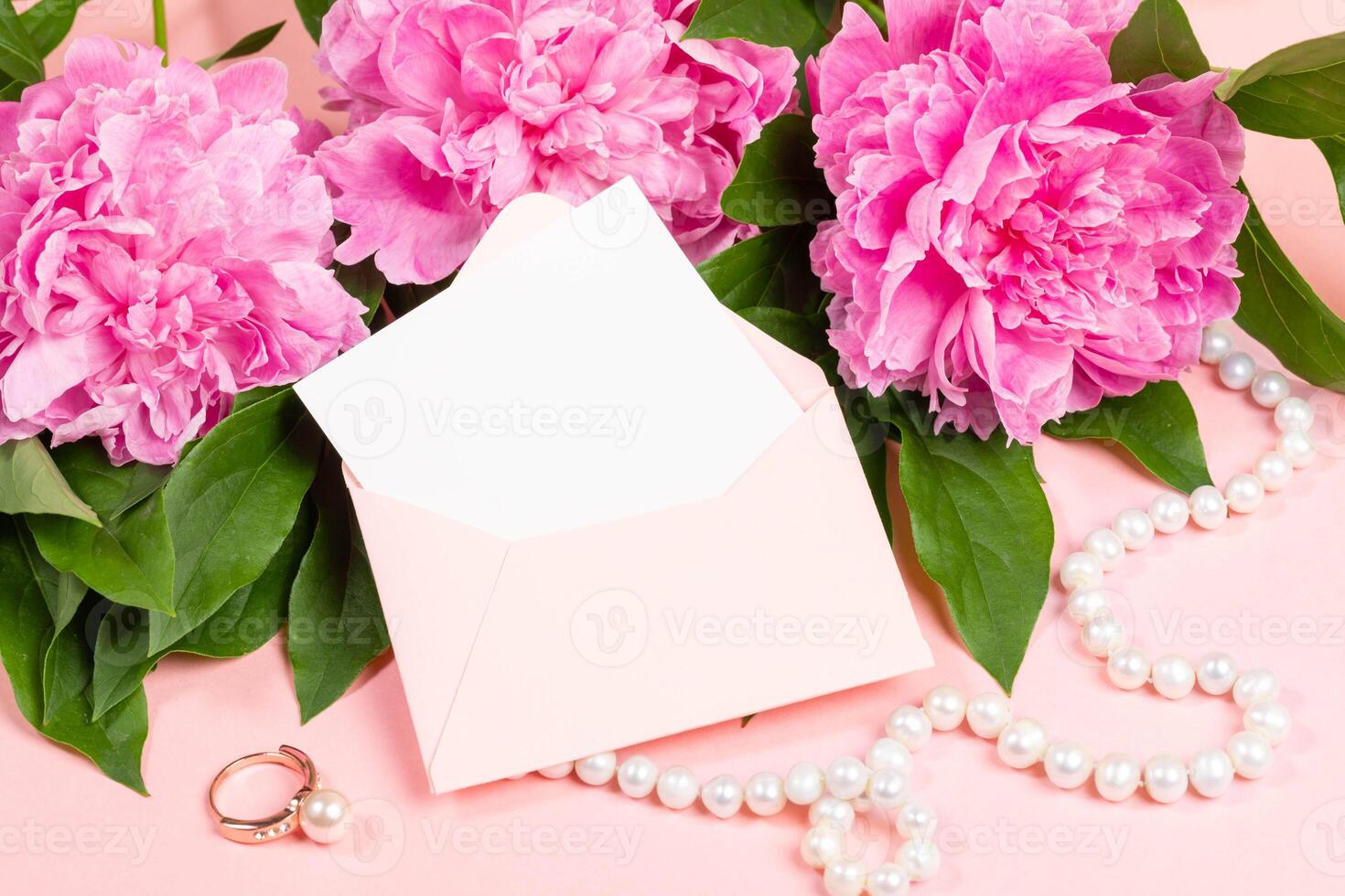 Festive flat lay with pink peonies, pearl necklace, ring and open envelope on soft pastel background photo