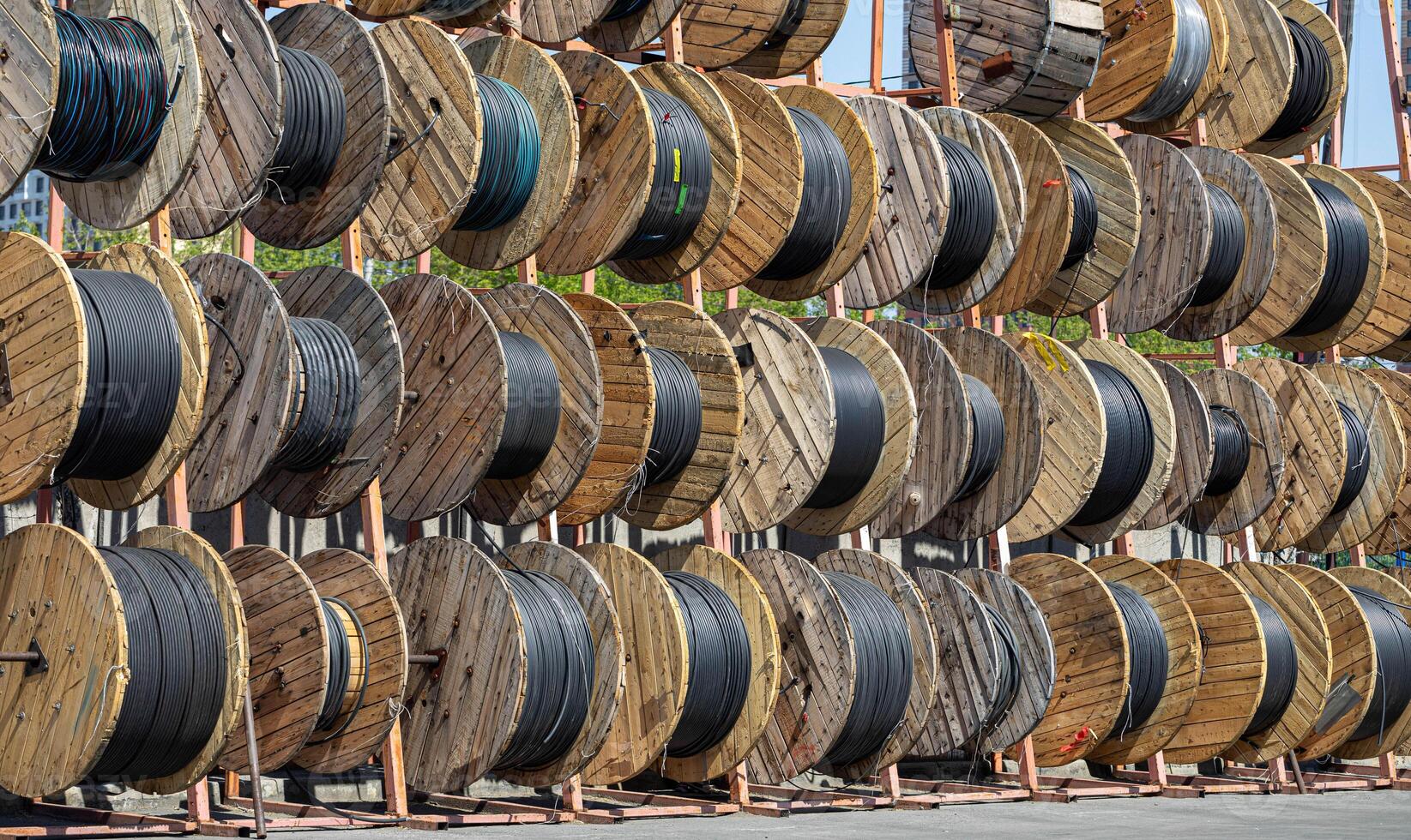 Wide view of storage of thick black industrial cable tightly coiled on wood reel at outdoor storage. photo