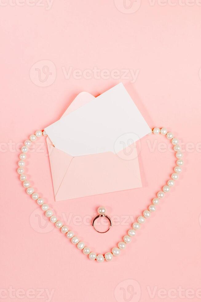 Stylized wedding layout with invitation, ring, pearl necklace shaped like heart on pink. Top view. photo