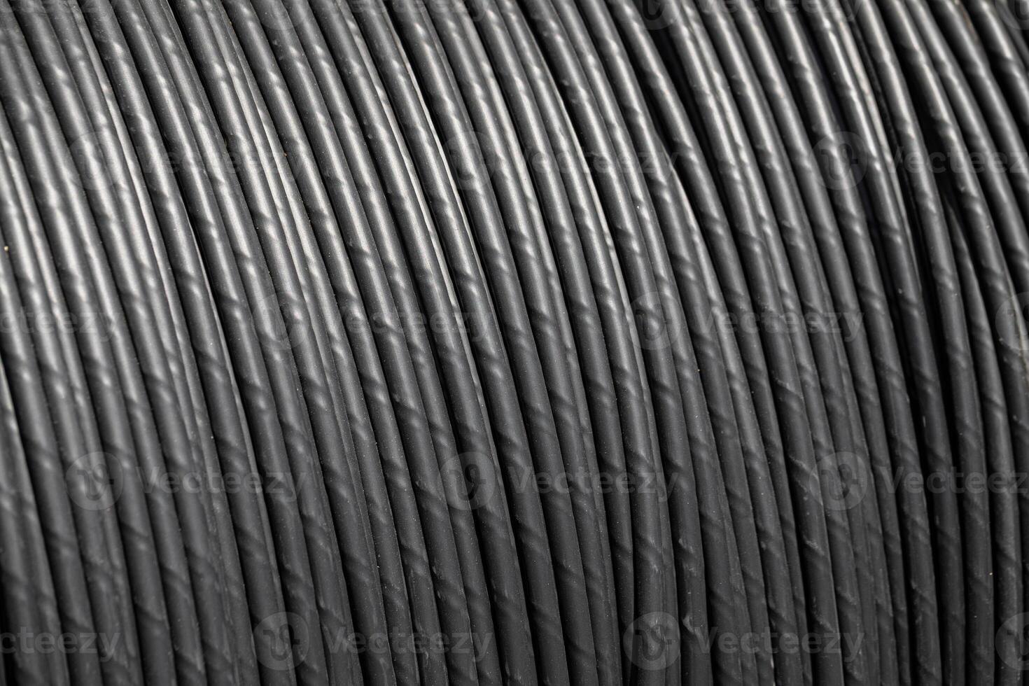 Close-up of thick black cable coil with visible grooves and shadows. Industrial wire texture. photo