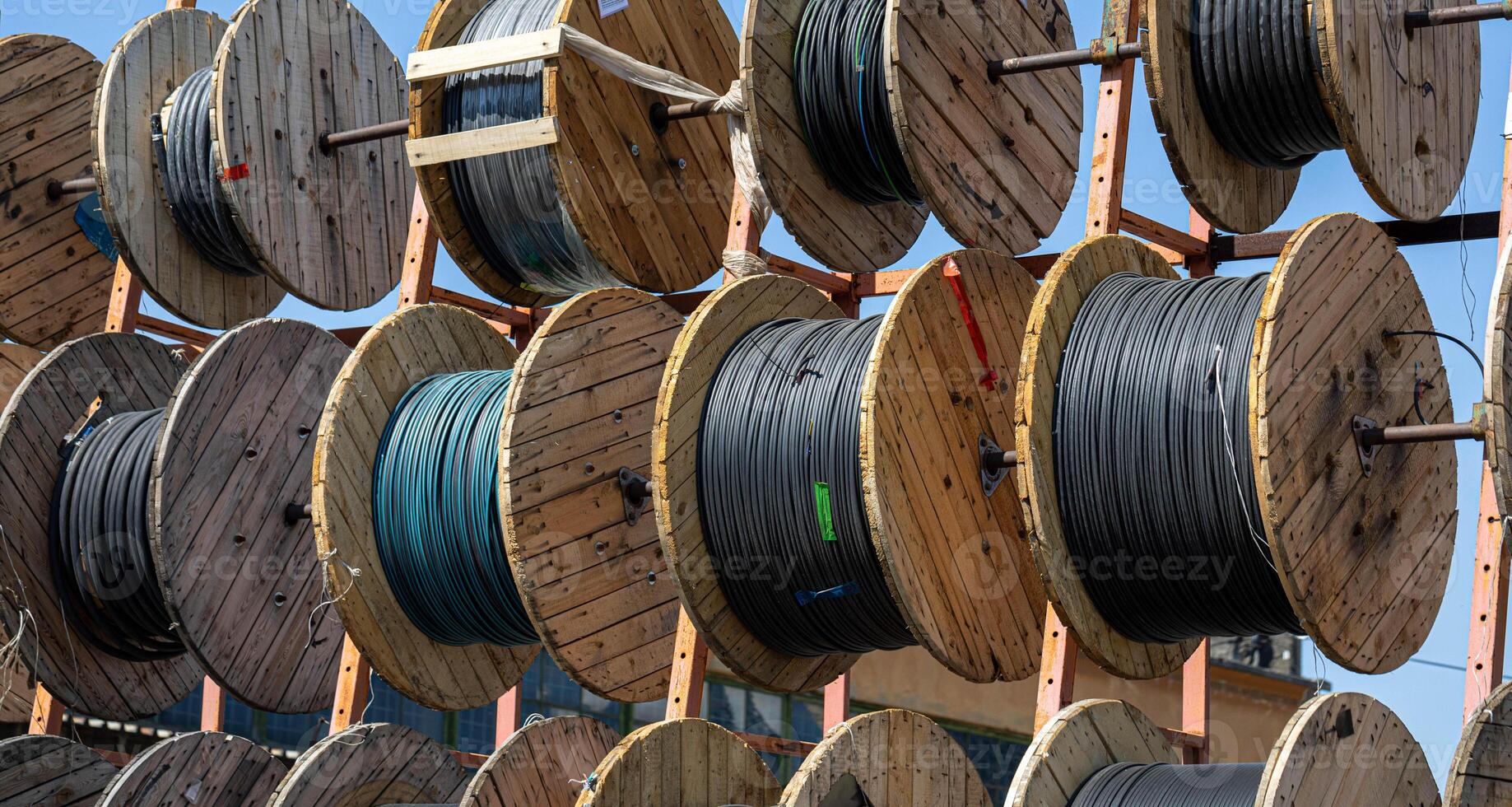 Multiple industrial cable reels stored outdoors, sunlight. Wooden spools are arranged in neat rows. photo