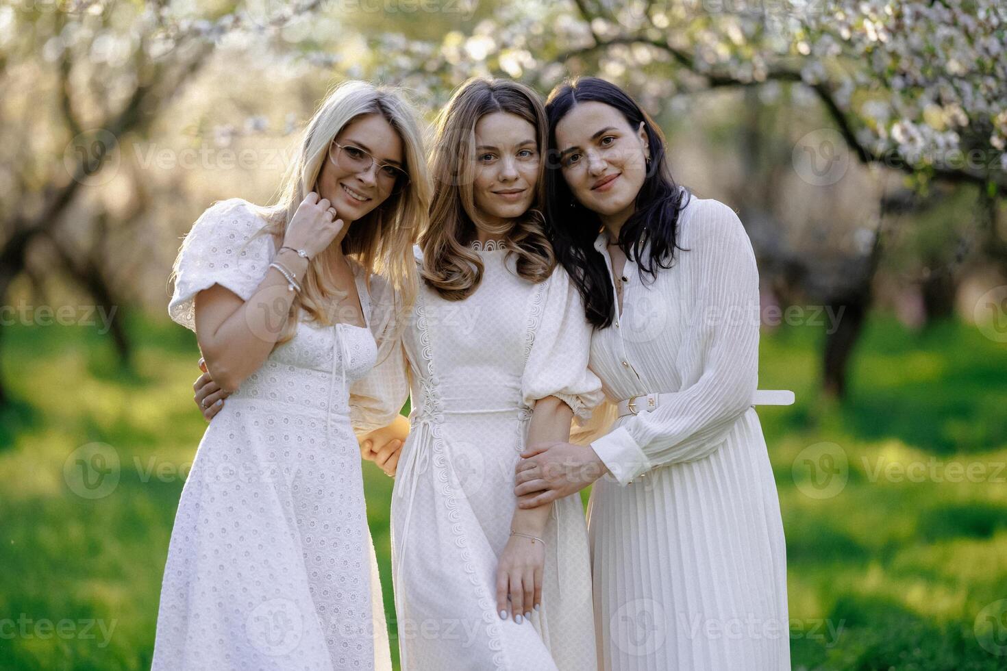 Three women in white dresses are happily posing in a park photo