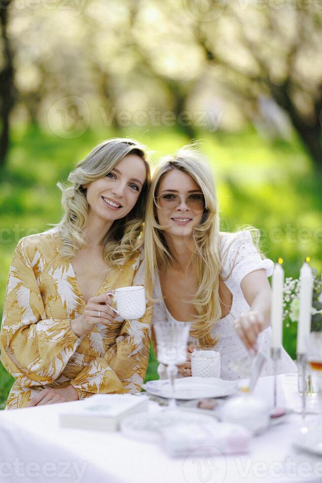 There are two women happily sitting at a table while holding cups of tea photo