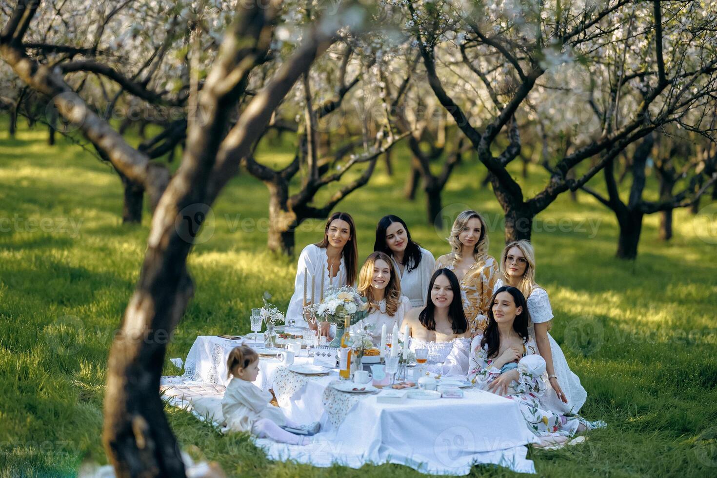 A group of women sits cheerfully around a table in a park photo