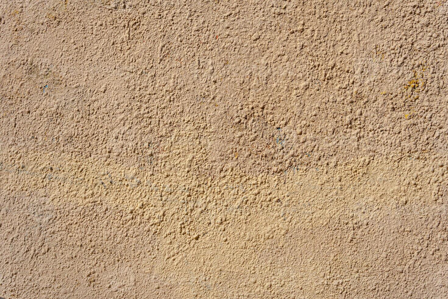 A yellow wall covered with numerous layers of plaster and paint. The layers form small irregularities and bumps. photo