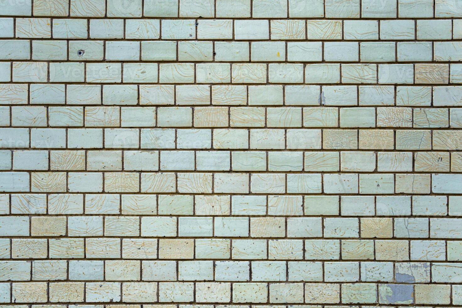 Wall of vintage bricks covered with cracked glaze. A wall with stains and cracks on the bricks. photo