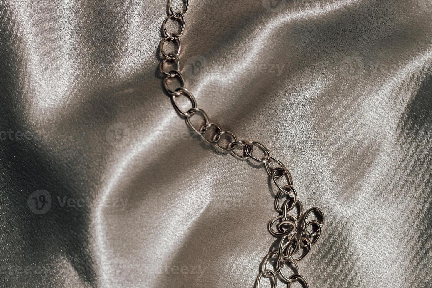 Silver chain laid on smooth satin fabric in softly lit environment photo