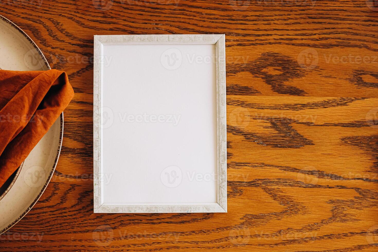 Elegant blank frame on wooden table beside a folded napkin in a minimalist setting photo