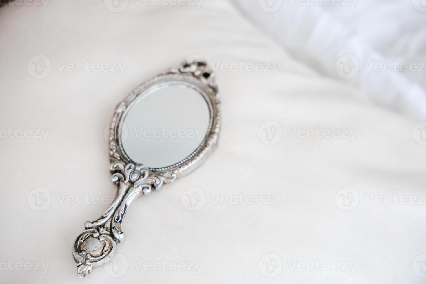 Vintage hand mirror placed elegantly on soft, white fabric in an intimate setting photo