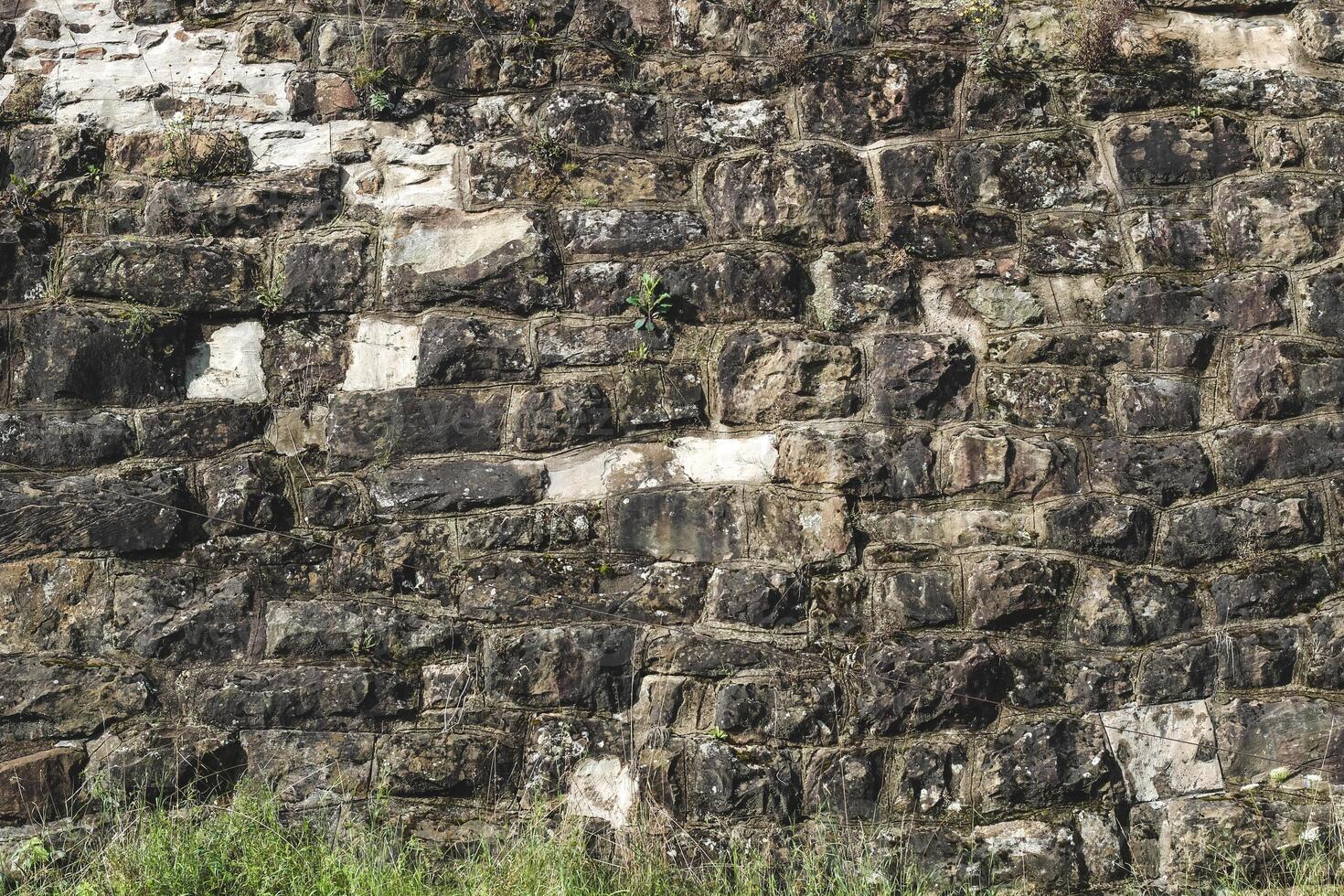 Texture of ancient stone wall covered with moss and grass in sunlight revealing history photo