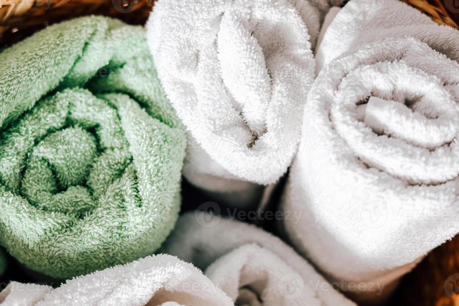 Freshly rolled green and white towels inside a woven basket at a spa or home setting photo